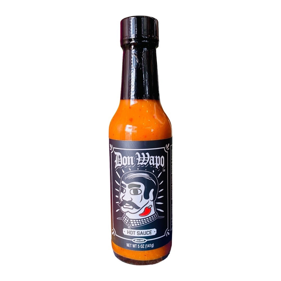 Front view of a glass bottle containing 5 oz of hot sauce. The label is black and features a graphic of a man with slicked back black hair, giant black eyebrows, a black mustache, and a red chili pepper tattoo on his neck. 