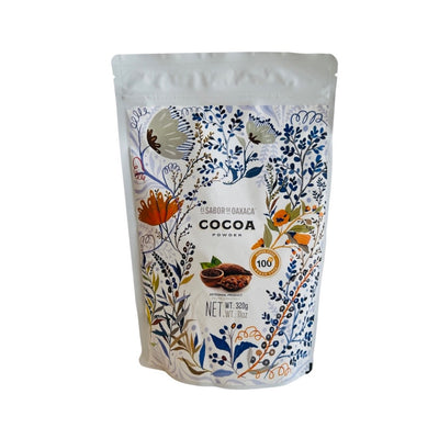 This bag of 11 oz of cocoa powder is ornately decorated with a white background and mostly blue flowers and vines and features an image of natural cocoa pods and a bowl of cocoa. 