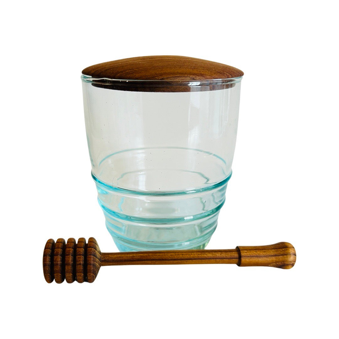 Single glass jar with a teak wood lid and a wooden honey dipper laying in the front of the jar.