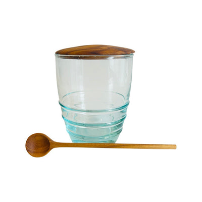 A single glass jar with a wooden lid and a wooden spoon laying in the front of the jar.