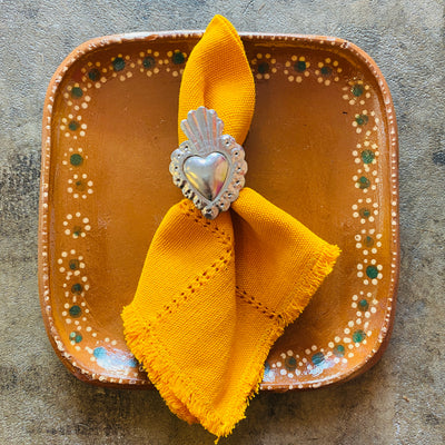 mustard colored Handwoven Cotton Napkin held together by silver heart shaped napkin ring holder at a meal place setting