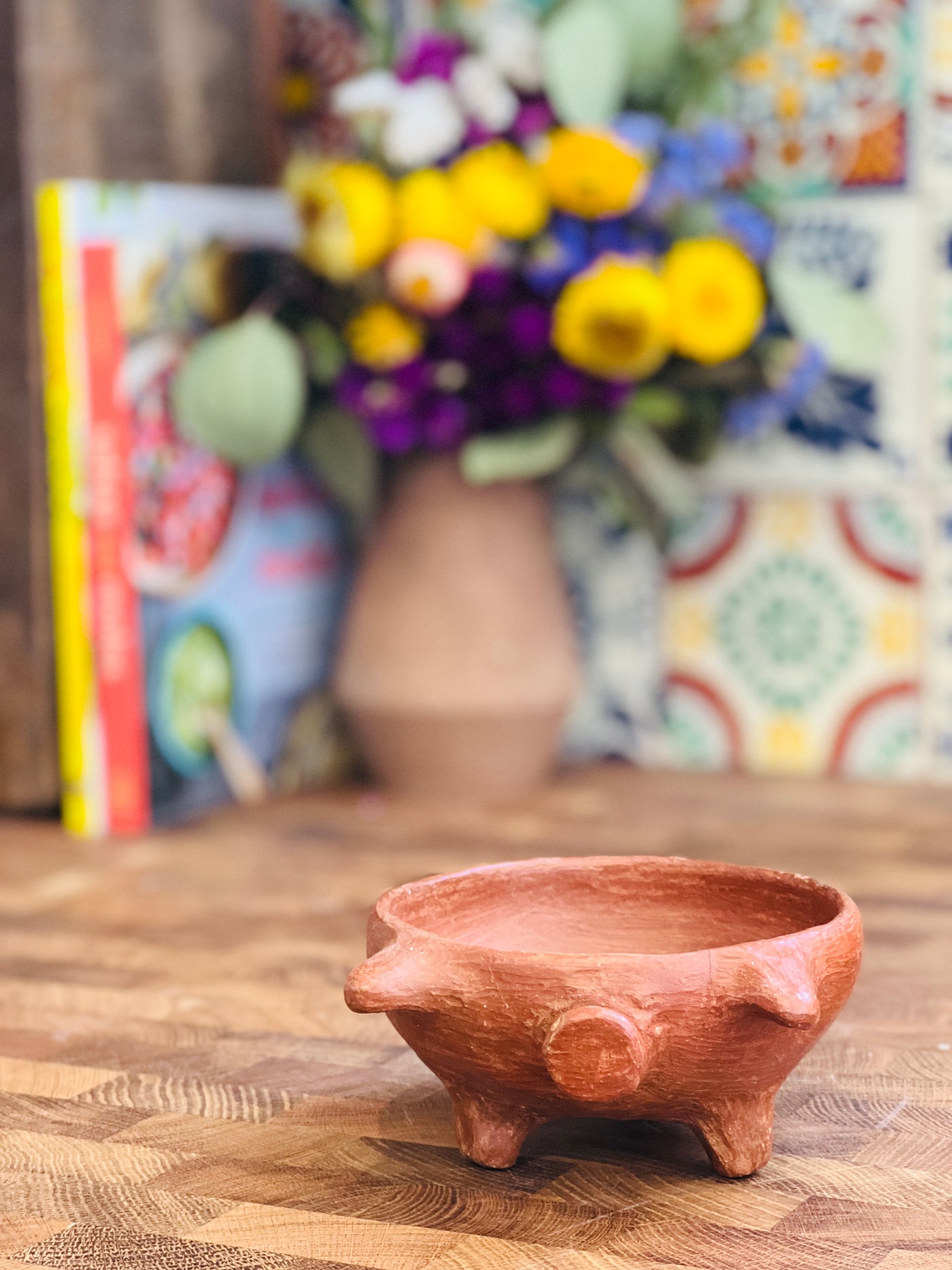 front view of red clay handsculpted bowl with pig legs and pig facial features in a kitchen setting