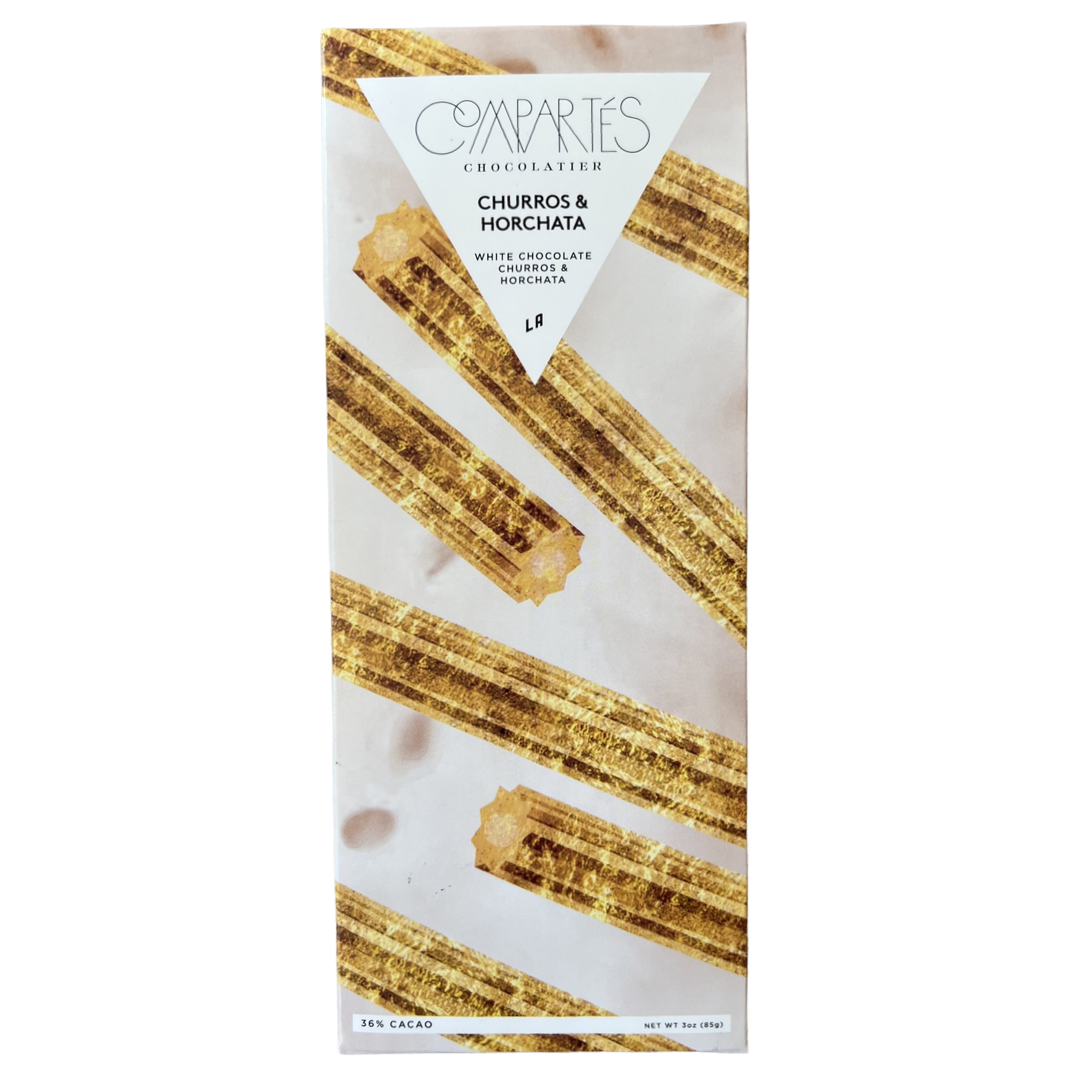 Front view of a 3 oz churro and horchata flavored chocolate bar with 36% cacao.  The packaging is white with gold glittery churros. 