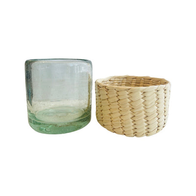 clear drinking glass sitting adjacent to palm woven koozie style cover