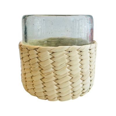 clear drinking glass sitting inside palm woven koozie style cover