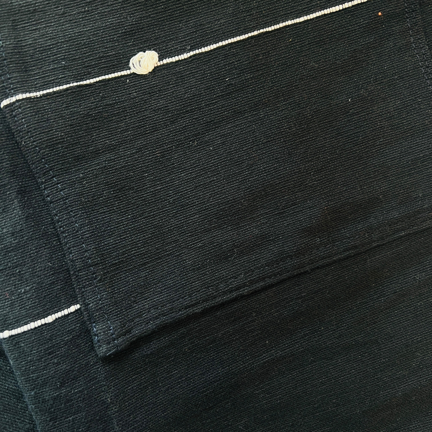 Close up of a black cotton woven apron with two front pockets