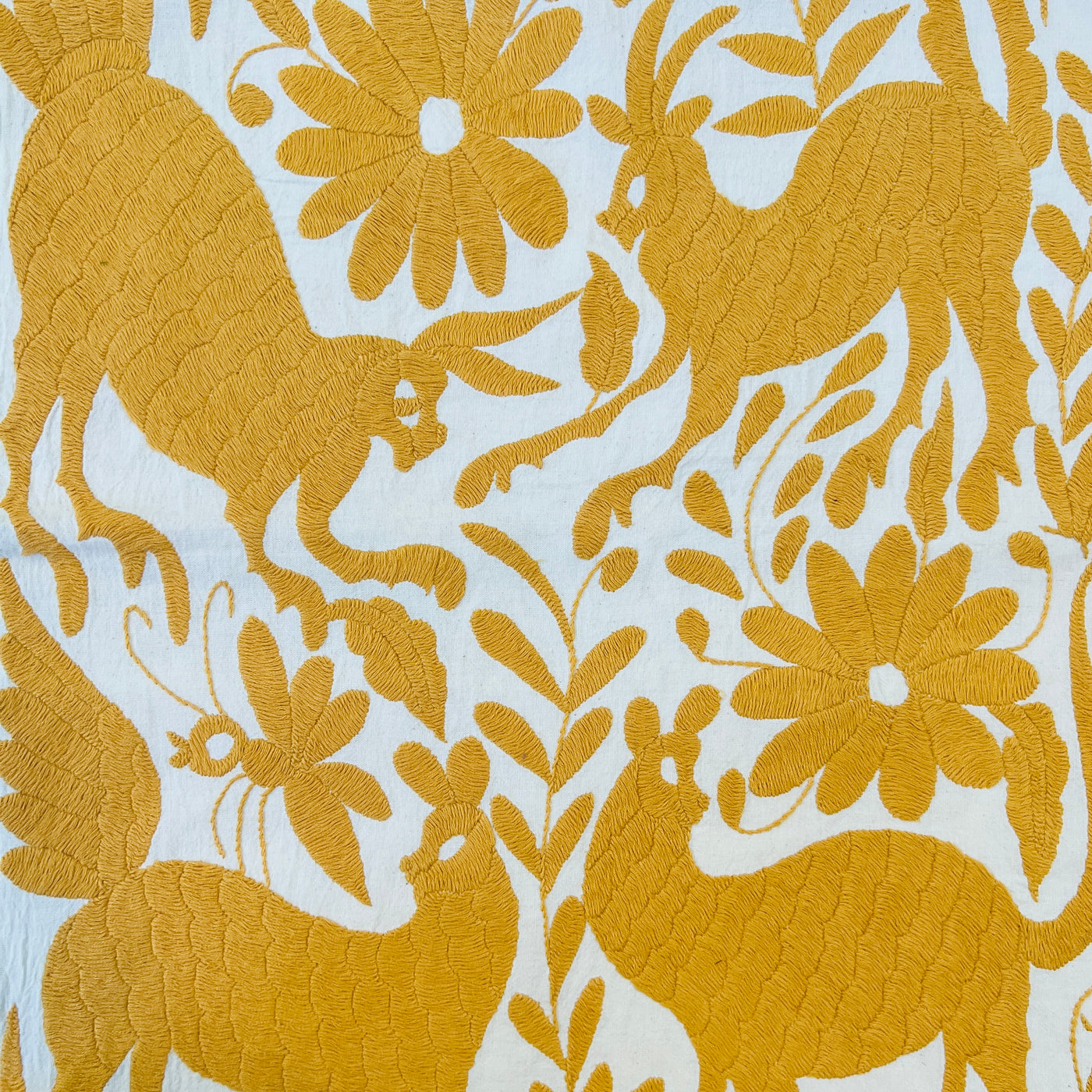 enhanced view of darker yellow floral and fauna scenery detail embroidered on off white table runner