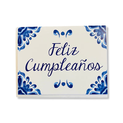 Greeting card reads: Feliz Cumpleanos, English translation is Happy Birthday. Illustration features talavera, traditional Mexican blue and white pottery design. Text is in cursive.