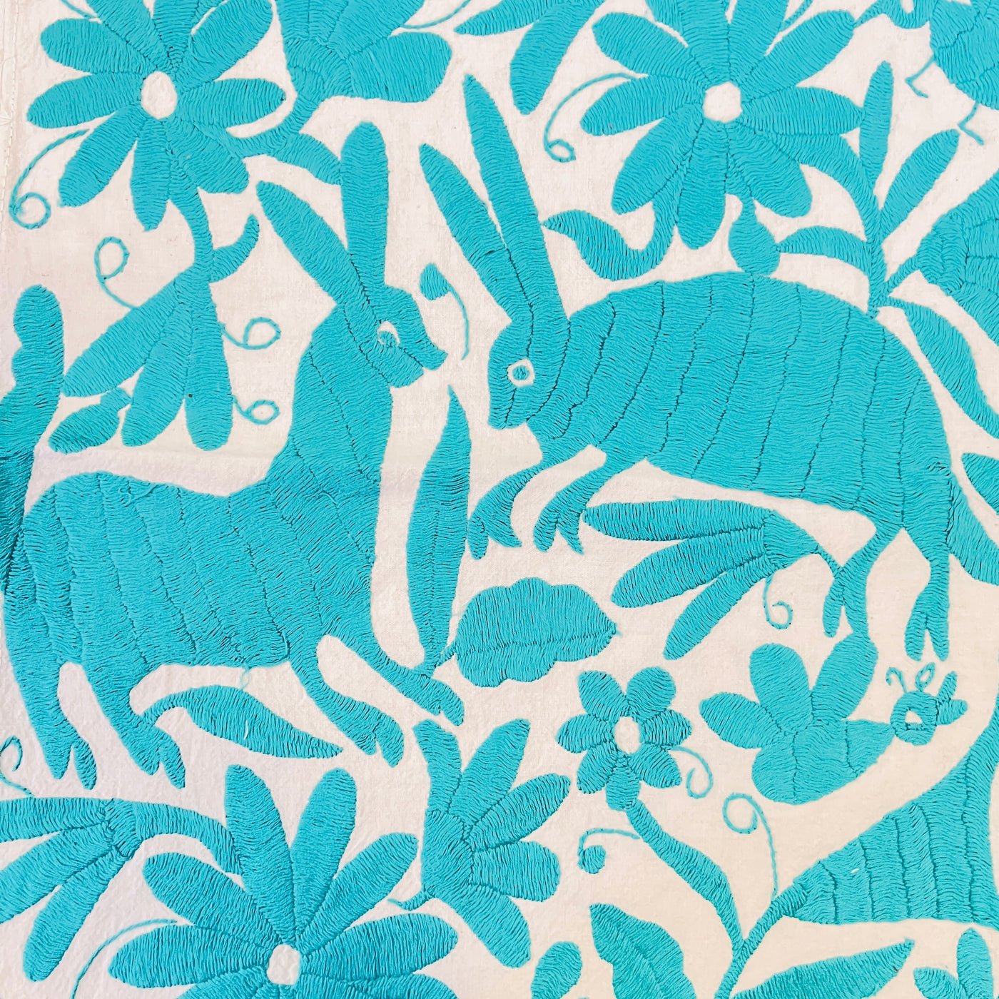enhanced view of turquoise floral and fauna scenery detail embroidered on off white table runner