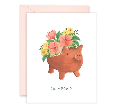 White card with a clay pig pot in the center with yellow and pink flowers and features the phrase Te Adoro. Translation: I adore you