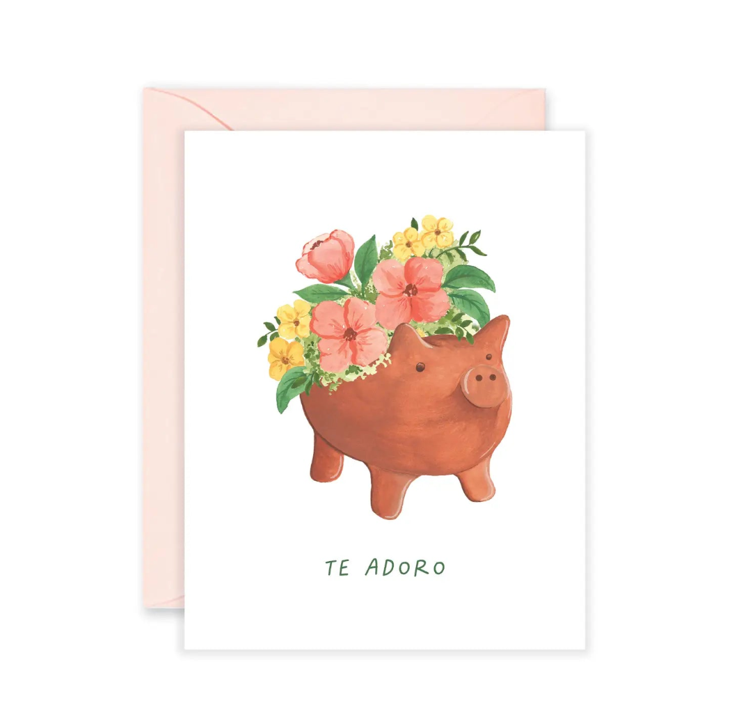 White card with a clay pig pot in the center with yellow and pink flowers and features the phrase Te Adoro. Translation: I adore you