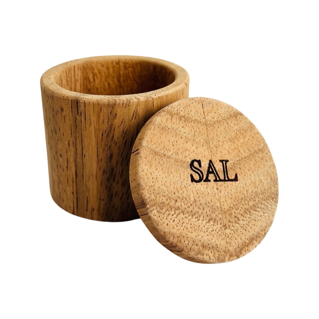 Light wooden salt box  with the Spanish word for salt, sal, engraved on the lid. The lid is leaning on the side of the salt box.
