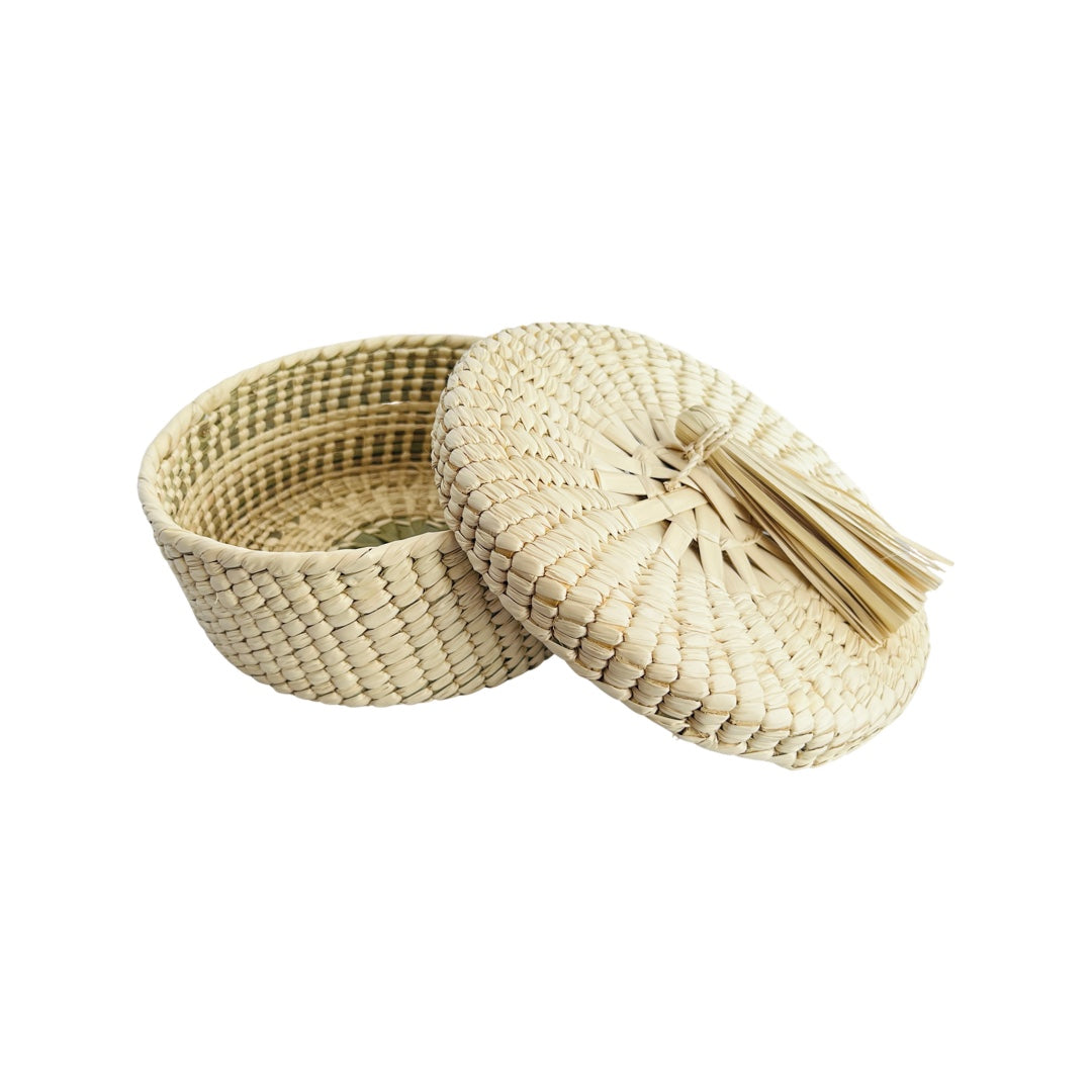 Mexican palm woven tortilla basket featuring a decorative palm tassle. The lid is off and leaning on the basket.