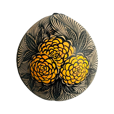 Half of a dried gourd painted black and engraved with a trio of orange marigolds and leaves.