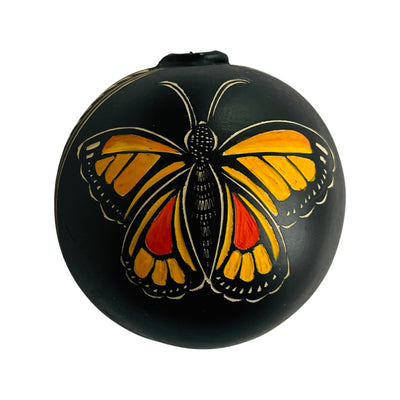 Half of a dried gourd painted black and engraved with a light and dark orange monarch design.
