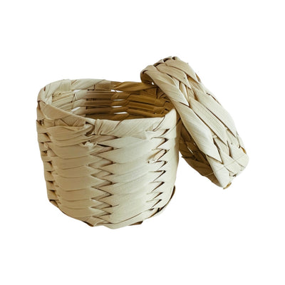 Front view of a natural palm woven basket with a lid leaning on the side of it.