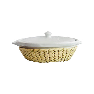 Side view of a white glazed barro casserole dish and lid with a palm leaf cover. 