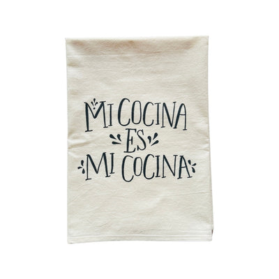 Natural flour sack kitchen towel with the phrase Mi Cocina Es Mi Cocina in black lettering. Translation: My Kitchen is My Kitchen.