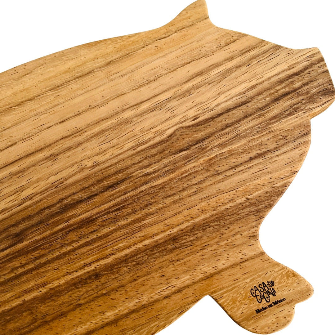 Close up view of a wooden pig shaped cutting board with the phrase Casa Y Cocina engraved on the front hoof. Translation for Casa y Cocina is Home and Kitchen. 