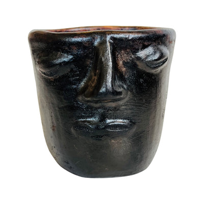 Front view of a Black clay mug with a face