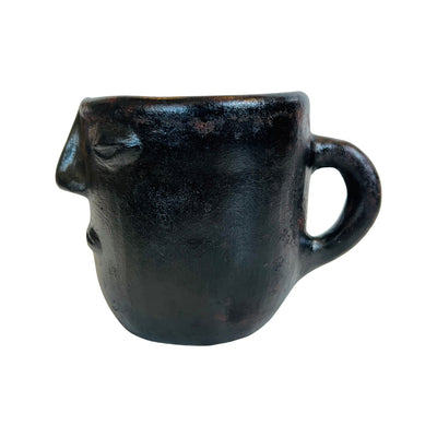 SIde view of a black clay mug with a face